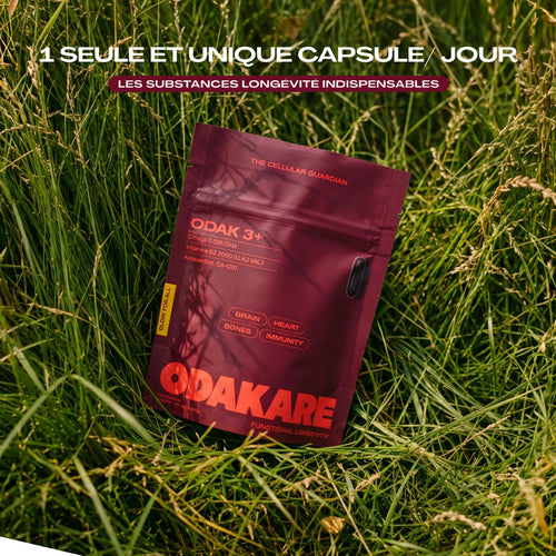 Sachet ODAK 3+ d’Odakare, couleur bordeaux, posé dans de hautes herbes vertes. Texte : « 1 seule et unique capsule par jour : les substances longévité indispensables »