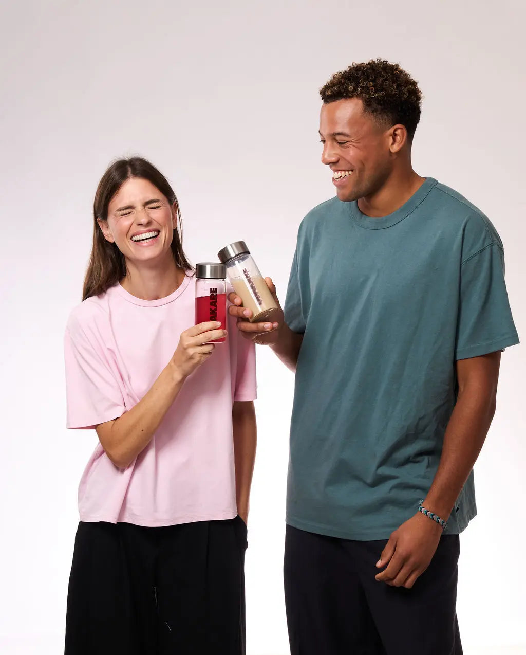Een vrouw en een man die het uitschateren en klinken met hun shakers van Odakare: de ene gevuld met een rode drank, de andere met een beige drank
